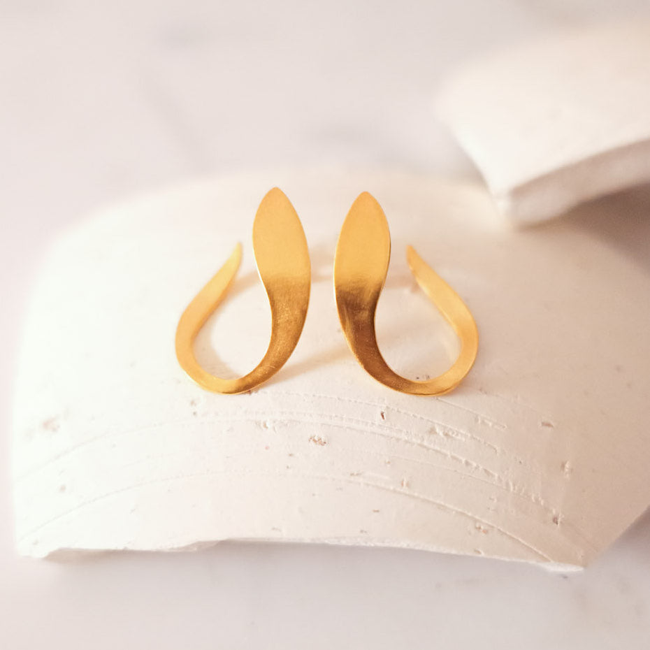 A pair of gold crescent-shaped hoop earrings displayed on a textured white ceramic dish against a light marble background.