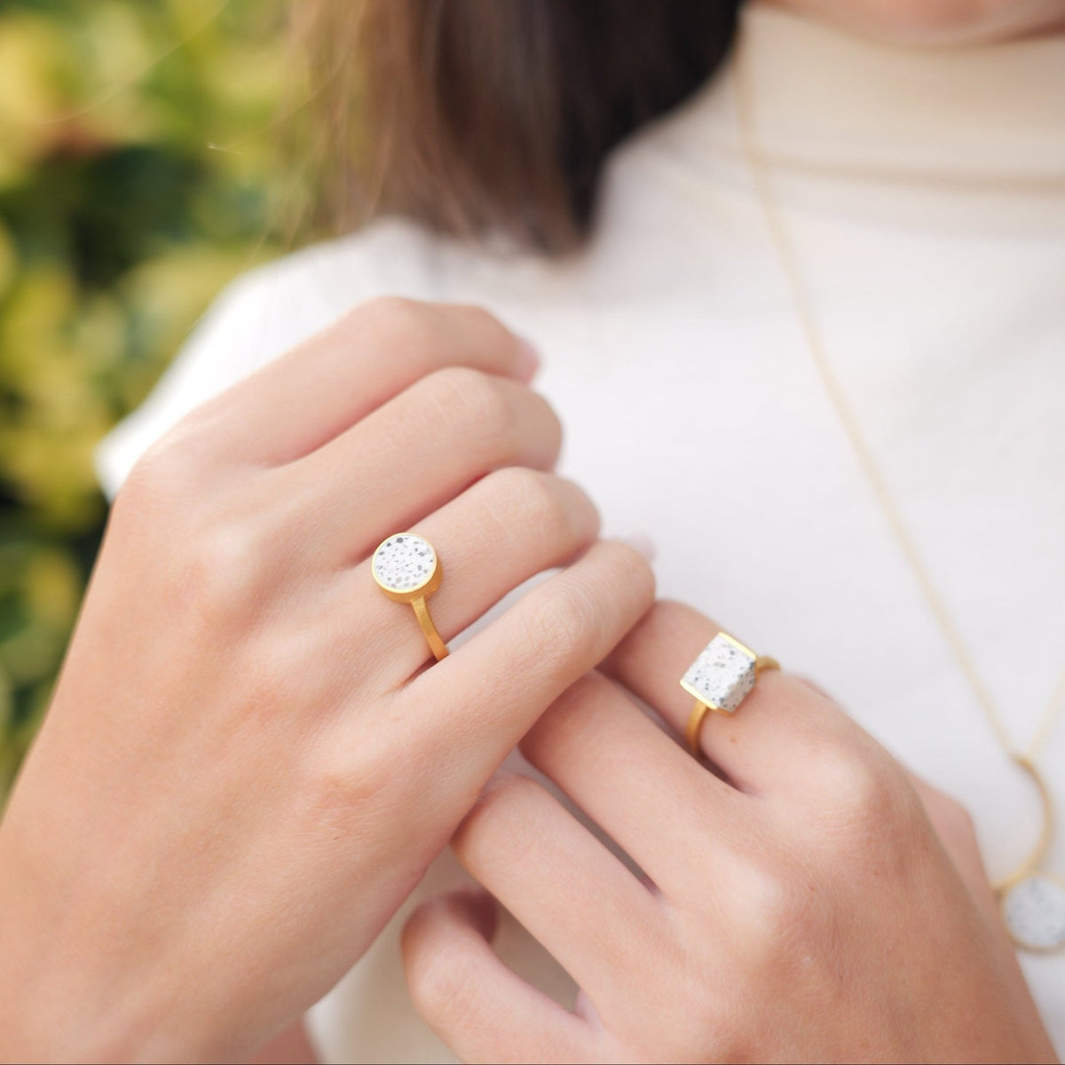 A woman wearing two gold rings with terrazzo stones, one round and one rectangular