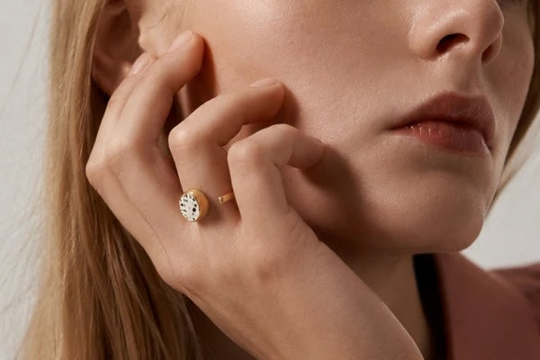 Close-up of a hand showcasing a contemporary terrazzo ring with a speckled ceramic centre and gold-plated band.